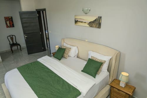 Lit tapissé crème avec literie verte à l'appartement La Villa des Pins à Akanda, Gabon
