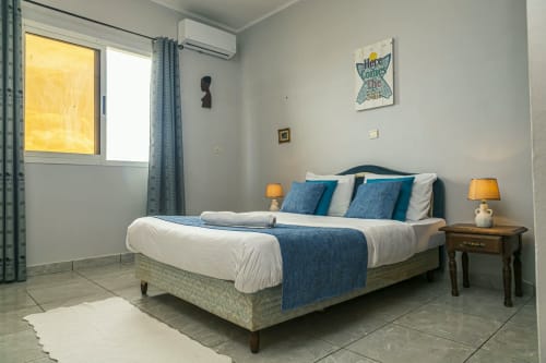 Chambre moderne à La Villa des Pins à Akanda avec literie bleue, lampes jumelées, climatisation et vue sur mer