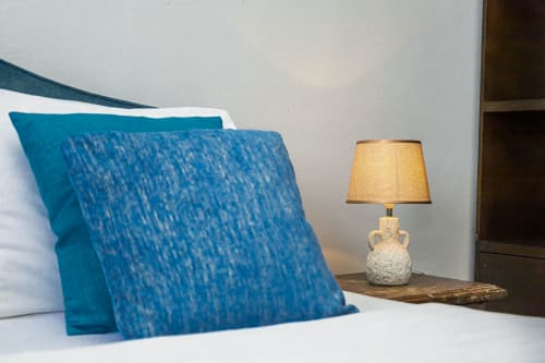 Chambre à La Villa des Pins avec coussins bleus texturés, lampe de chevet abat-jour crème, décor moderne et vue mer