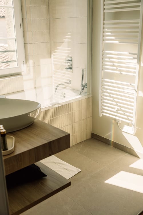 Salle de bains moderne et lumineuse au Château Alto Cormeil à Saint-Émilion avec baignoire spa, sèche-serviettes électrique et lumière naturelle