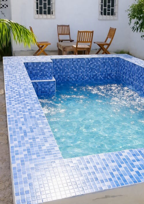 Piscine de la Villa des Pins à Akanda avec carrelage mosaïque bleu, transats en bois et cour aux murs blancs