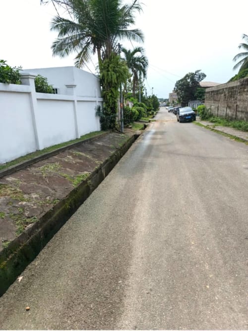 Allée pavée de La Villa des Pins à Akanda avec villa blanche, palmiers et voitures garées