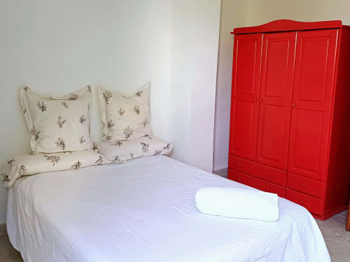 Dormitorio luminoso en Hacienda Blanca Marbella con ropa de cama blanca, almohadas florales, armario rojo y toalla blanca
