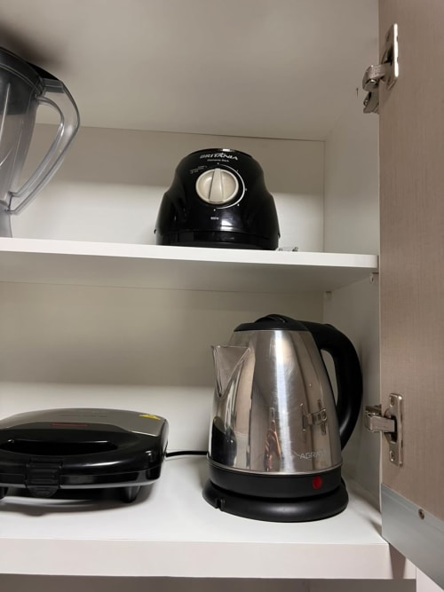 Cozinha compacta com chaleira elétrica e máquina de café em prateleiras brancas na BORA BORA HOSPEDAGENS, Joinville