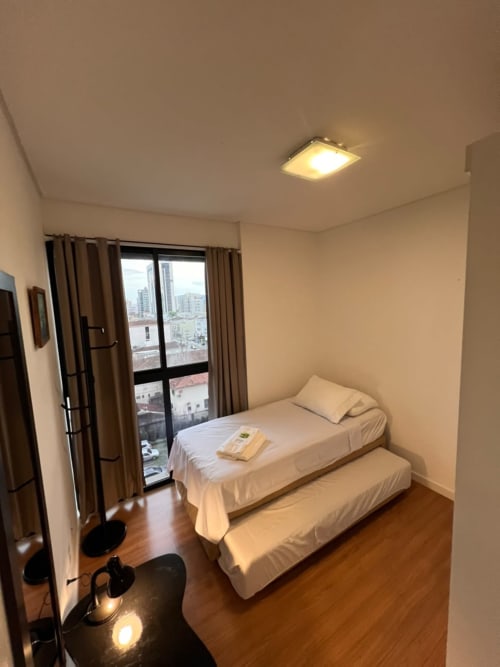 Quarto moderno com camas de solteiro, vista da cidade da varanda, piso de madeira na Bora Bora Hospedagens em Joinville