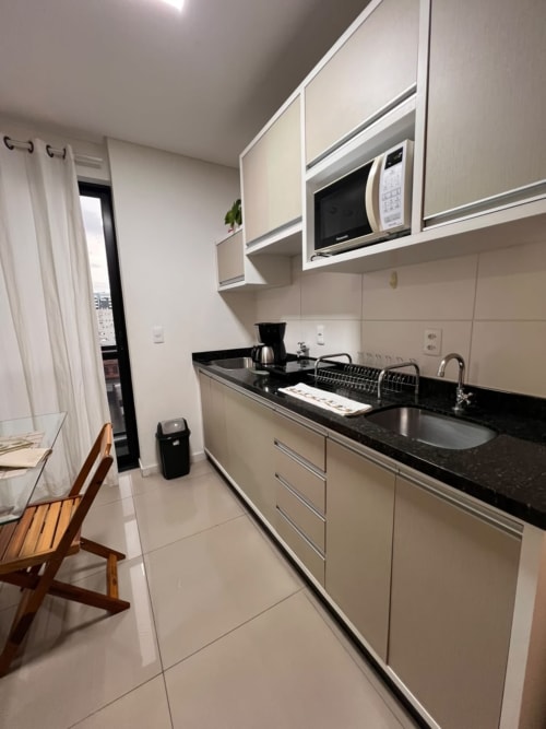 Cozinha moderna em apartamento de Joinville com bancada preta, armários brancos, micro-ondas e eletrodomésticos em aço inoxidável