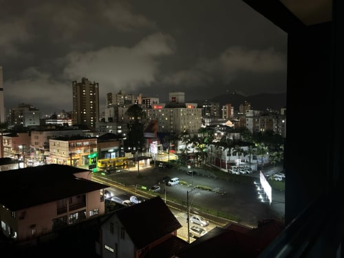 Vista noturna da paisagem urbana de Joinville da sacada do apartamento BORA BORA, destacando edifícios iluminados do centro e ruas