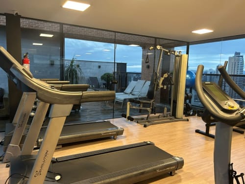 Academia moderna com esteiras e equipamentos de musculação com vista para o horizonte de Joinville a partir de prédio residencial