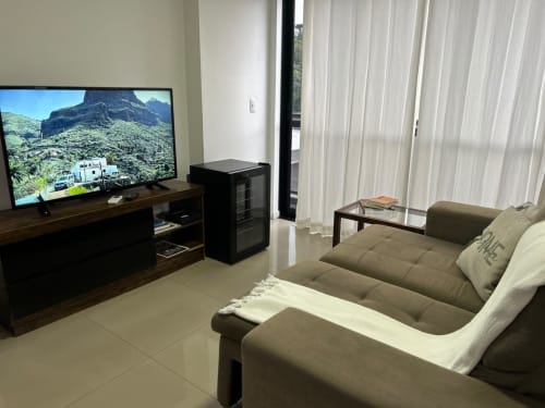 Sala de estar moderna em apartamento em Joinville com TV de 50 polegadas, sofá cinza, mesa de vidro e vista para a cidade