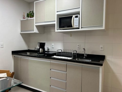 Cozinha moderna em apartamento Duplex na BORA BORA HOSPEDAGENS, Joinville com bancada preta, armários bege, micro-ondas e