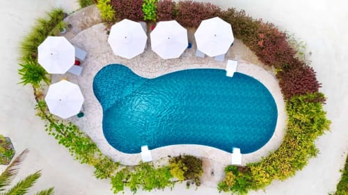 Aerial view of OPOA Beach Hotel's pool in Uturoa with white umbrellas, loungers, and tropical landscaping