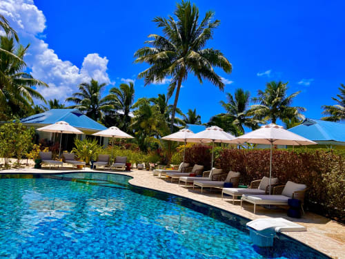 Piscine avec vue lagon de l'hôtel OPOA Beach, palmiers, chaises longues, parasols et bungalows à Uturoa, Polynésie française