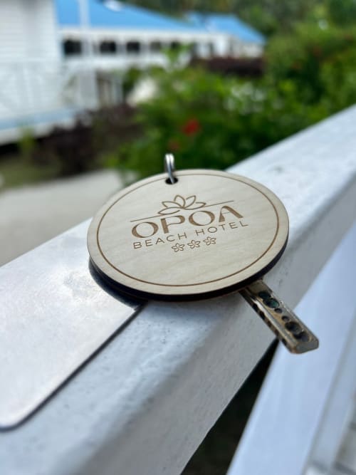 OPOA Beach Hotel wooden key tag resting on white lounge chair with tropical resort in background, Uturoa