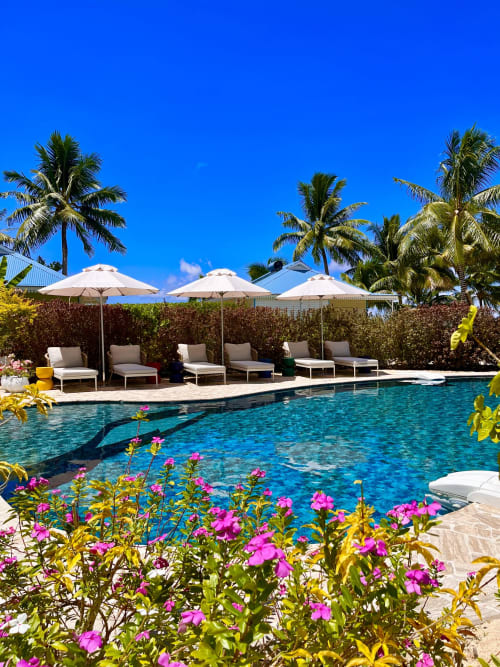 Luxury pool area at OPOA Beach Hôtel in Uturoa with turquoise water, lounge chairs, white umbrellas, palm trees, and vibrant