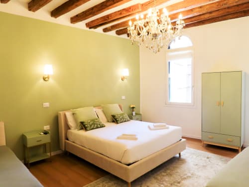 Bright yellow bedroom in Verona with cream bed, crystal chandelier, wooden beams, and river view window