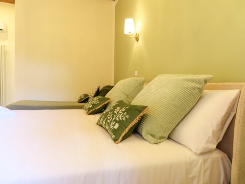 Elegant bedroom in San Marco Luxury Suite, Verona with yellow walls, white linens, and decorative pillows near river view