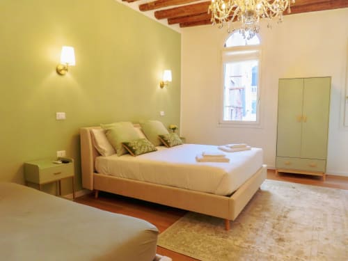 Luxurious bedroom in Verona with yellow walls, cream bed, chandelier, and arched window overlooking the canal