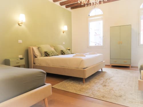 Luxury bedroom suite in Verona with yellow accent wall, elegant bed, wardrobe, and arched window with river view