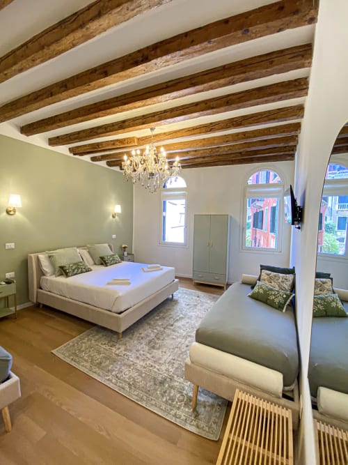 Luxurious superior suite in Verona with exposed beams, chandelier, canal view, and dual beds with green accents