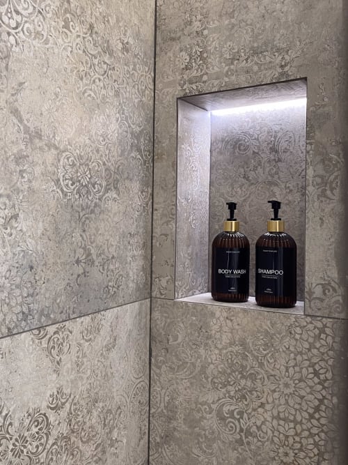 Luxury bathroom niche with illuminated recessed shelf displaying premium body wash and shampoo bottles, Verona hotel suite