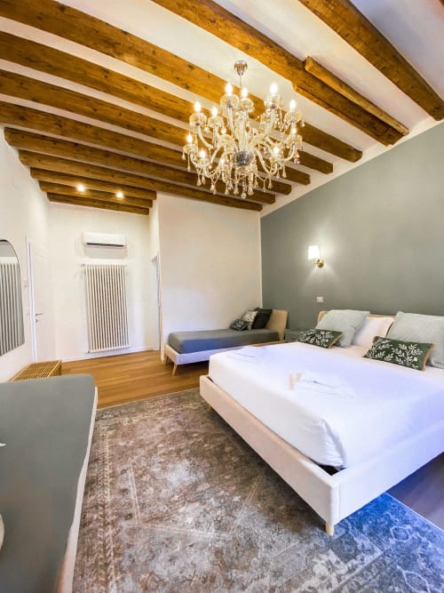 Luxurious Verona suite with exposed wooden beams, crystal chandelier, queen bed with river view, and elegant furnishings