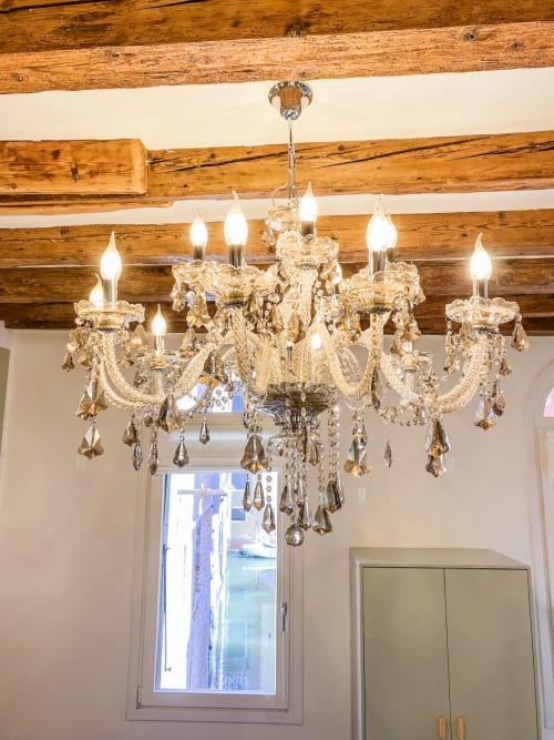 Elegant golden chandelier with crystal drops hanging from rustic wooden beams in Verona luxury suite