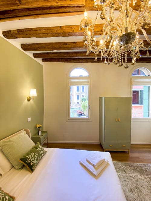 Luxurious Verona suite with exposed beams, crystal chandelier, green accent wall, arched windows with canal views, and