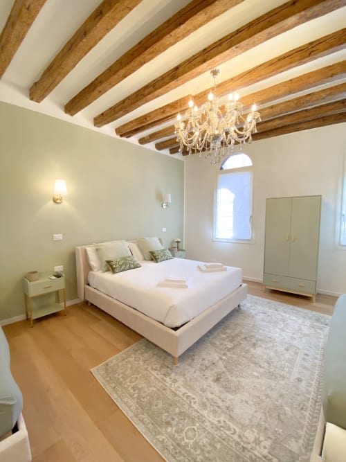 Elegant bedroom suite in Verona with exposed wooden beams, crystal chandelier, white bed, and arched window with canal view