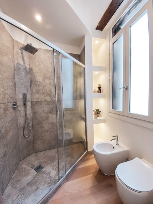 Modern bathroom with walk-in shower, rainfall showerhead, white sink and toilet, wooden flooring, and illuminated built-in