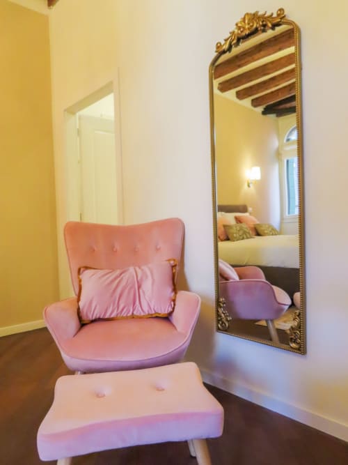 Pink velvet armchair with ottoman near ornate gold mirror in luxurious Verona suite with yellow walls and wooden beams