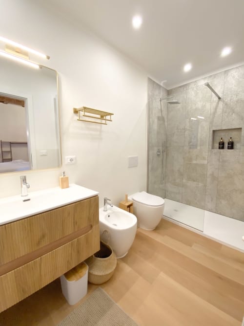 Modern luxury bathroom with wooden vanity, white fixtures, rainfall shower with gray tile, and heated towel rack at San Marco