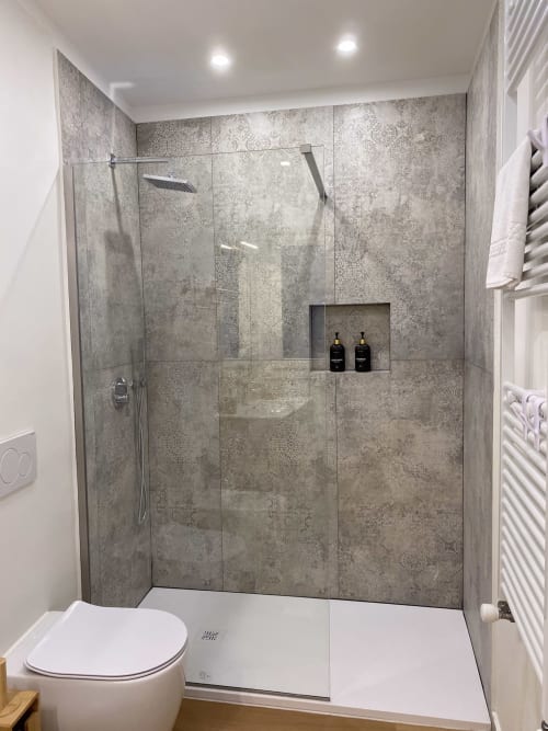 Modern shower enclosure with gray marble-pattern tiles, rainfall showerhead, and built-in niche at San Marco Luxury Suites in
