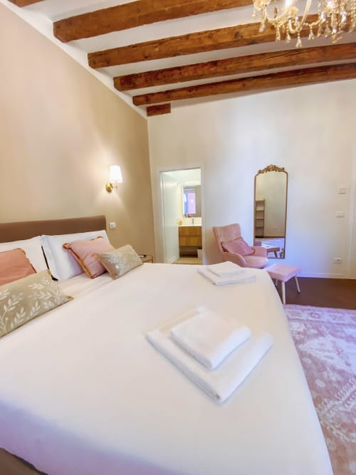 Luxurious Verona suite bedroom with exposed wooden beams, white walls, elegant furnishings, pink accents, and river view
