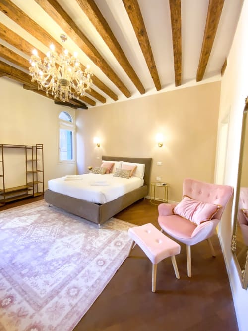 Luxury suite bedroom in Verona with exposed wooden beams, gray bed, pink armchair, and river view window
