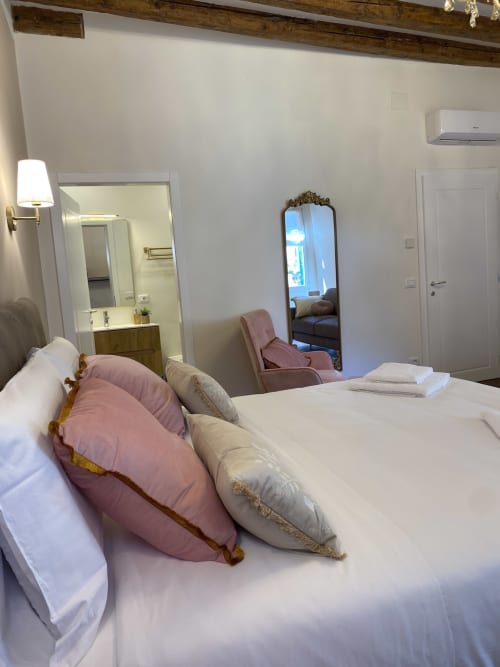 Luxury suite bedroom in Verona with elegant white bedding, pink and cream pillows, ornate mirror, and river view amenities.