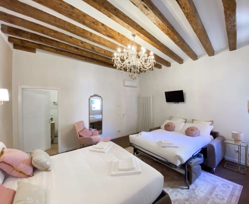 Luxurious suite in Verona with exposed wooden beams, crystal chandelier, two beds, and modern amenities