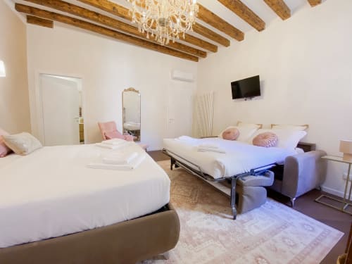 Luxurious Verona suite with two beds, exposed wood beams, chandelier, mirror, and wall-mounted TV