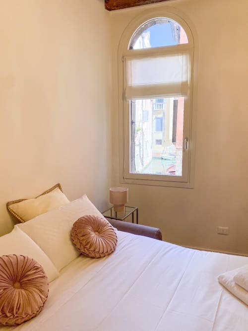 Bright bedroom in Verona suite with canal view, cream bedding, decorative pillows, and arched window overlooking canal
