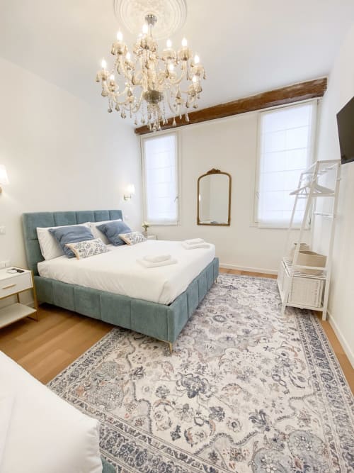 Luxurious bedroom in Verona hotel with teal upholstered bed, crystal chandelier, ornate mirror, and period beams