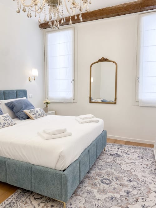 Elegant bedroom in San Marco Luxury Suites, Verona with blue upholstered bed, crystal chandelier, ornate mirror, and classic
