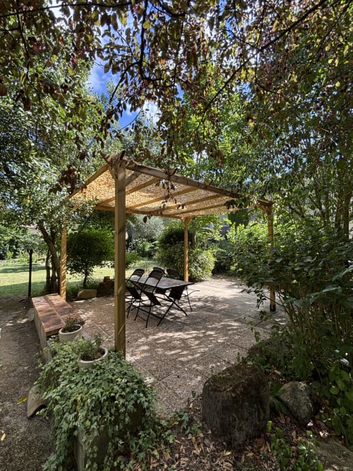 Pergola en bois avec coin détente ombragé entouré d'une verdure luxuriante à la Guesthouse Le Cocon De Curson