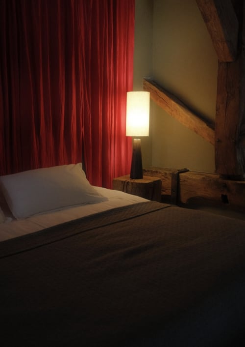 Modern bedroom at Moulin Renaudiots Autun with illuminated bedside lamp, red curtains, and rustic wood beams