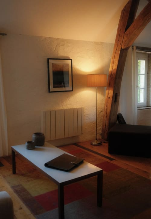 Cozy living room at Moulin Renaudiots with warm lighting, wooden beams, radiator, and modern furnishings overlooking the