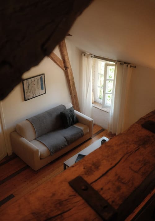Cozy loft bedroom at Moulin Renaudiots in Autun with cream sofa, exposed beams, wooden floors, and garden view doors
