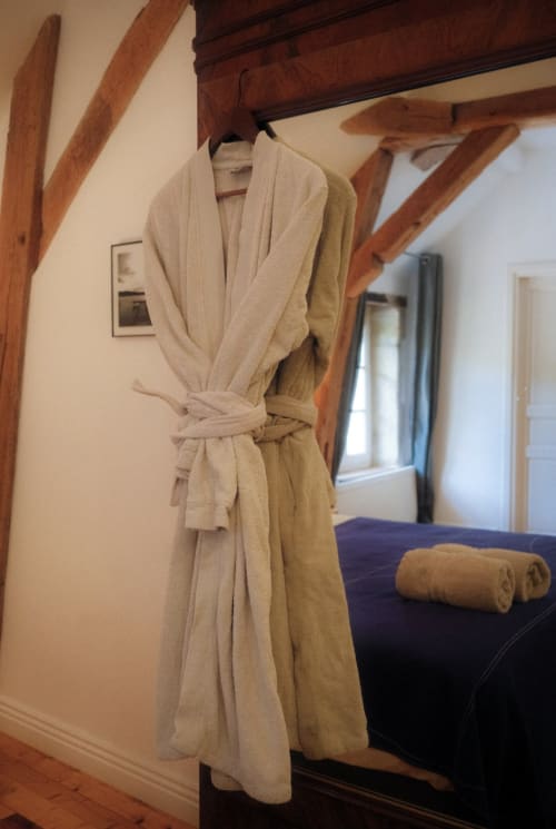 Cream-colored bathrobe hanging on wooden beam in Rolin room at Moulin Renaudiots, Autun
