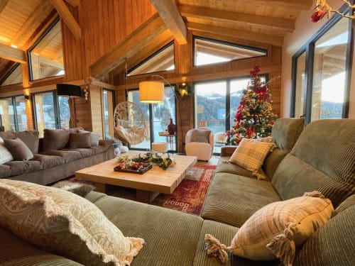 Salon de chalet de luxe à La Plagne avec vue montagne, poutres apparentes, décoration de Noël et sièges confortables