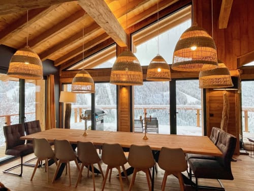 Salle à manger de luxe en chalet montagnard avec luminaires suspendus tissés, poutres en bois et vue sur les Alpes enneigées aux Chalets