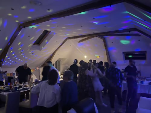 Les invités se mélangent dans l'espace événementiel moderne des Gites De Flaubert, éclairé par une ambiance lumineuse bleue et verte vibrante
