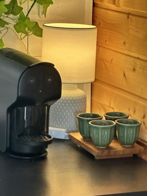 Cafeteira e xícaras verdes estampadas na mesa de madeira da pousada Monte da Tojeiranha com iluminação ambiente