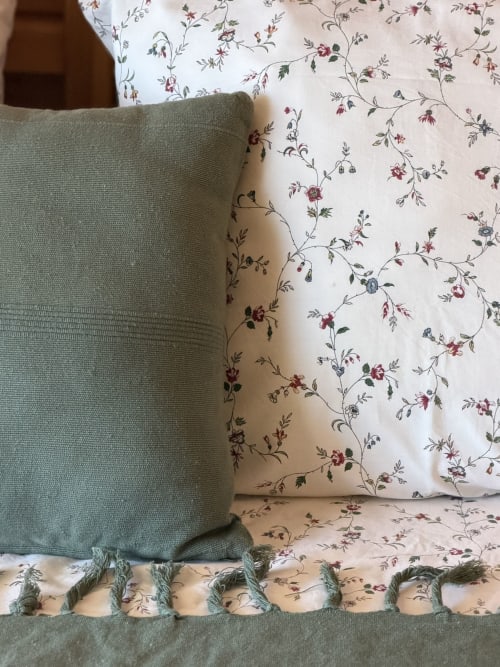 Almofada verde sálvia com borlas sobre roupa de cama com padrão floral no bungalow Monte da Tojeirinha, Montargil